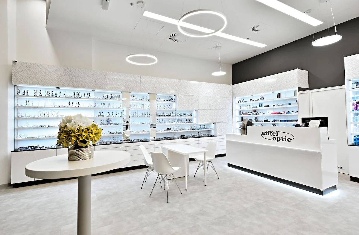 Interiér druhé optiky s pokladnou a posezením, laděno do bílé barvy