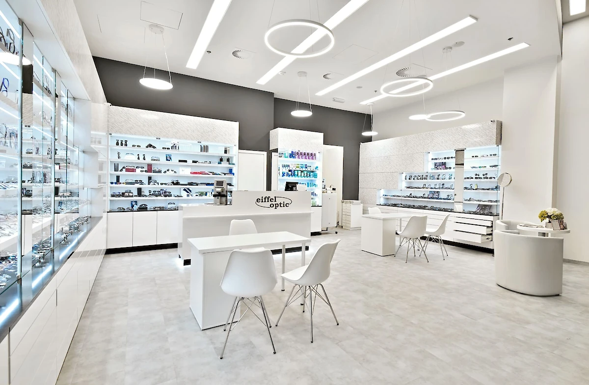 Interiér druhé pobočky optiky, vitríny a bílý stůl se židlemi