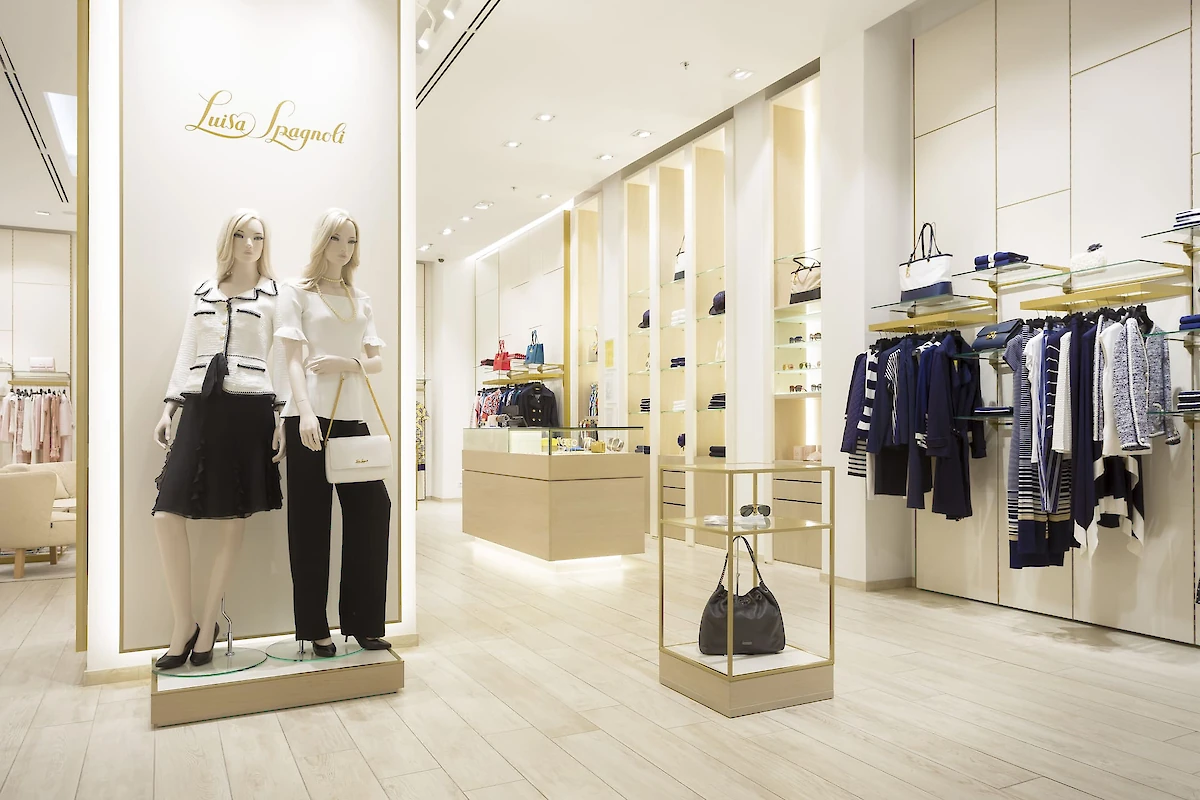 Interiér butiku s oblečením a doplňky: figuríny, věšákové systémy a police s oblečením, pokladna