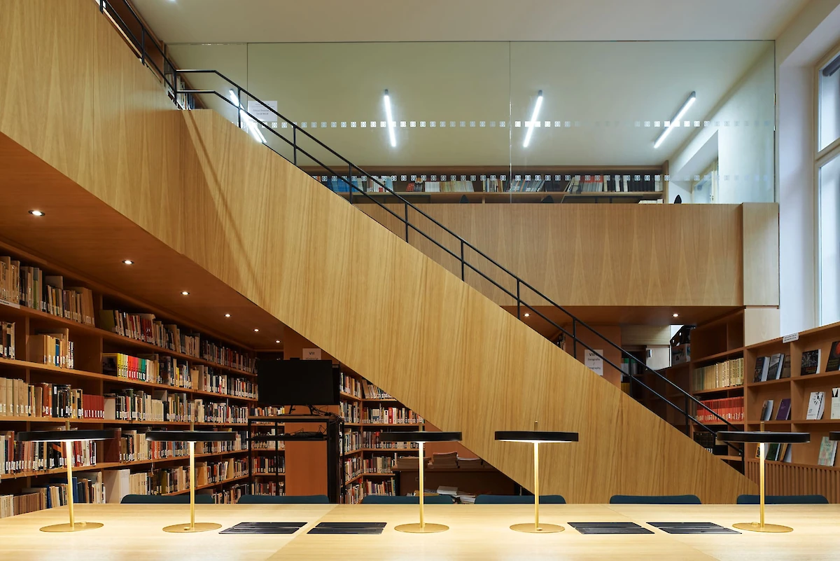 Interiér knihovny s výrazným dřevěným schodištěm
