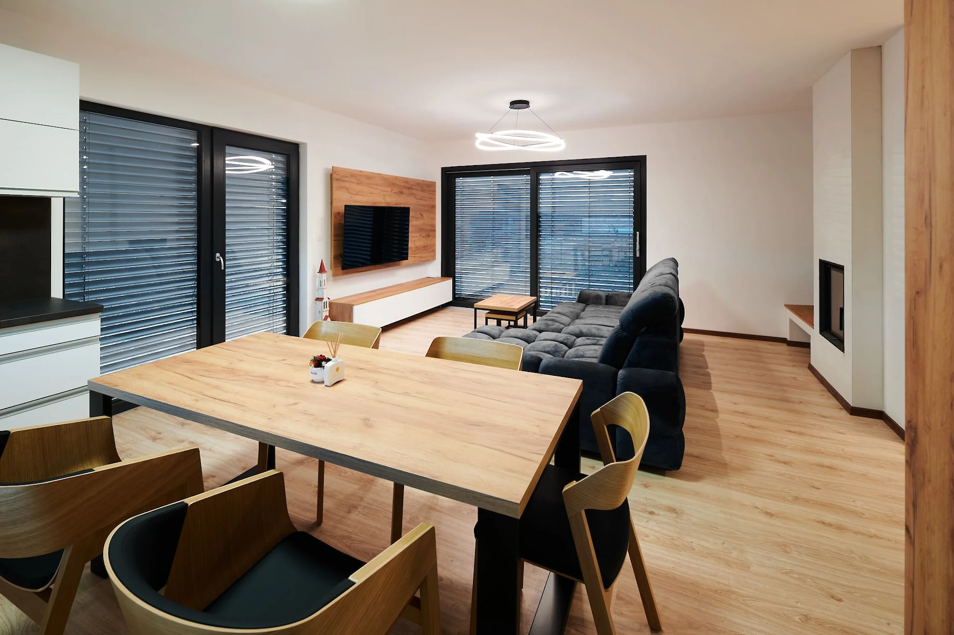 Jídelna a obývám - dřevěný stůl se židlemi, velká šedá pohovka a televizní stěna