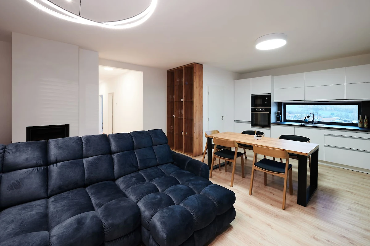 Velká šedá pohovka, stůl se židlemi, kuchyně